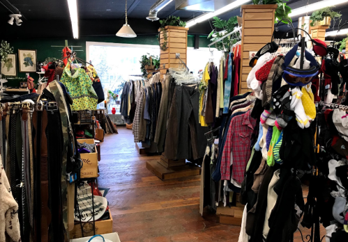 A vintage clothing store aisle filled with racks of clothes, accessories, and a cozy, inviting atmosphere.