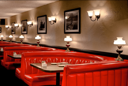Cozy diner interior with red booths, vintage lamps, and framed black-and-white photos on the walls.