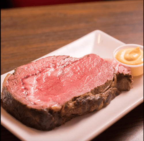 A juicy slice of prime rib served on a plate with a side of creamy sauce.