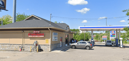 A fast-food restaurant named Jay's Chicken next to a gas station, with cars parked outside and a clear blue sky.