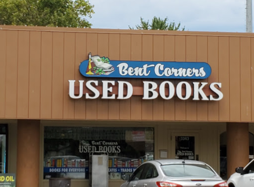 Sign for "Bent Corners Used Books" on a storefront, featuring books and a welcoming design.