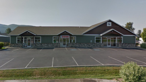 A green building with a stone facade, featuring large windows and a sign that says "BOOKS," set in a parking lot.
