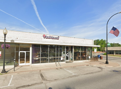 Exterior of a restaurant with large windows, an American flag, and hanging flower baskets on a sunny day.