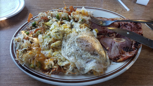 A plate of breakfast featuring scrambled eggs, hash browns, and slices of ham.