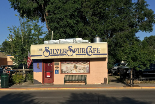 A small café building with a sign reading "The Silver Spur Café," surrounded by trees and parked cars.