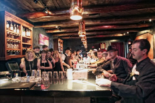 A lively bar scene with a diverse group of people gathered around the counter, enjoying drinks and conversation.