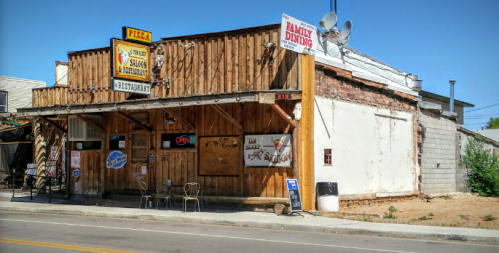 A rustic pizza restaurant with wooden exterior, open sign, and outdoor seating on a sunny day.