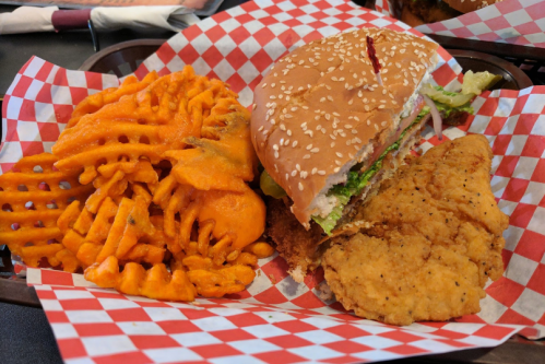 A plate with a sesame seed burger, lettuce, and a side of crispy waffle fries.
