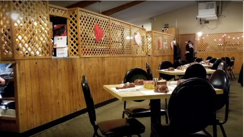 Interior of a restaurant with wooden lattice dividers, tables set for dining, and staff interacting in the background.