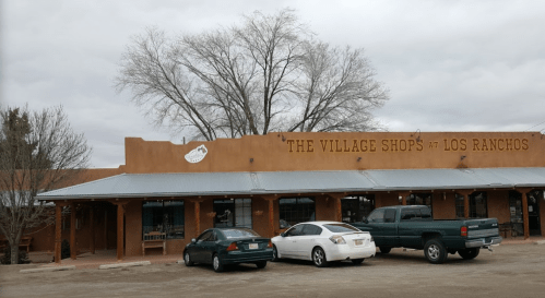 Exterior of "The Village Shops at Los Ranchos," featuring a southwestern-style building and parked cars.