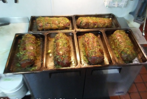 Six trays of marinated meatloaf, garnished with herbs, resting on a kitchen counter.