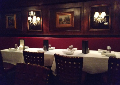 Elegant restaurant interior with a white tablecloth, candles, and framed artwork on dark wood walls.