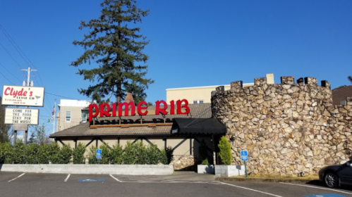 Exterior of Clyde's restaurant featuring a stone wall and a prominent "Prime Rib" sign. Trees and a parking area visible.