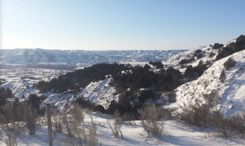 Snow-covered hills and valleys under a clear blue sky, showcasing a serene winter landscape.