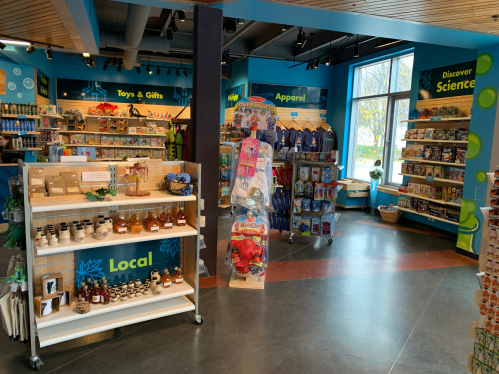 A brightly lit store interior showcasing shelves of toys, gifts, apparel, and local products.