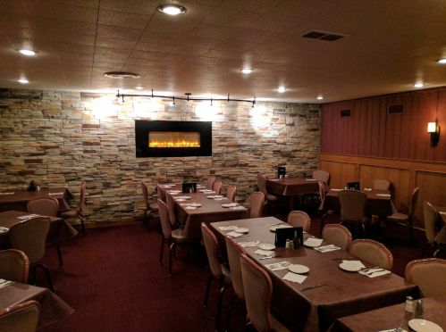 Cozy restaurant interior with stone wall, tables set for dining, and a modern fireplace as a focal point.