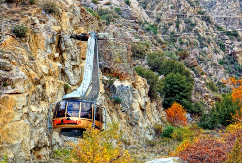 A cable car glides over rocky terrain, surrounded by autumn foliage and steep cliffs.