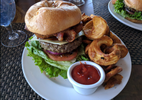 A hearty burger with bacon, cheese, lettuce, and tomato, served with curly fries and a side of ketchup.