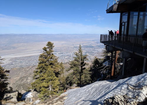 A scenic view from a mountain overlook, showing a valley below with trees and a building on the edge.