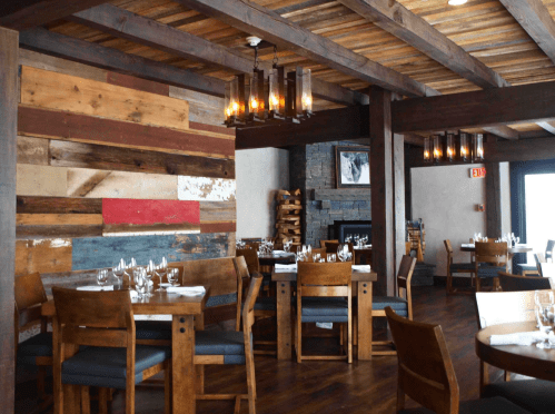 Cozy restaurant interior featuring wooden beams, rustic decor, and tables set for dining. Warm lighting enhances the ambiance.
