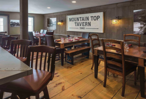 Cozy restaurant interior with wooden tables, chairs, and a vintage sign reading "Mountain Top Tavern 1940."