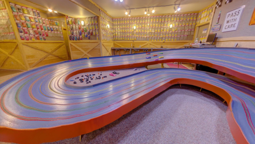 A colorful slot car track with multiple lanes, surrounded by walls adorned with toy car displays.