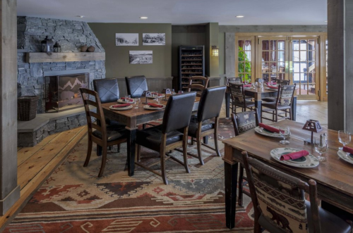 Cozy dining area with wooden tables, leather chairs, a stone fireplace, and rustic decor.