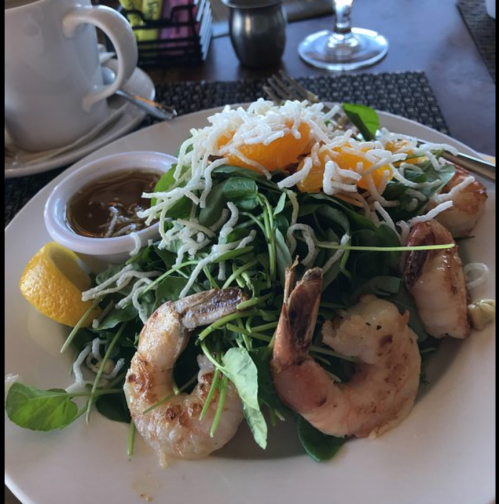 A fresh salad topped with shrimp, shredded coconut, and orange segments, served with a lemon wedge and dipping sauce.