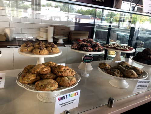 Display of various cookies on white pedestals, including funfetti, stuffed, and chocolate varieties.