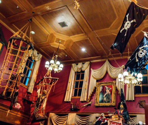A pirate-themed room with hanging nets, skull flags, chandeliers, and a portrait on the wall.