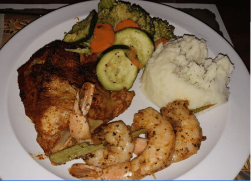 A plate of grilled chicken, shrimp skewers, mashed potatoes, and steamed vegetables including broccoli and carrots.