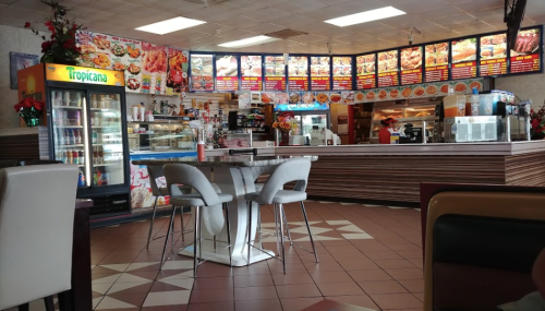 Interior of a casual restaurant with colorful menu boards, a drink cooler, and a table with chairs.