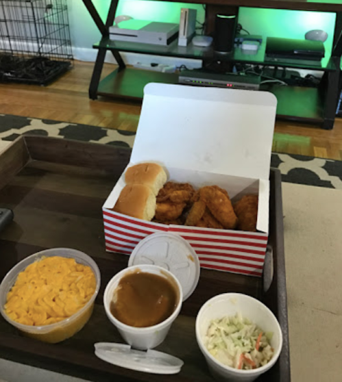 A takeout meal featuring fried chicken, two buns, macaroni and cheese, coleslaw, and gravy on a wooden tray.