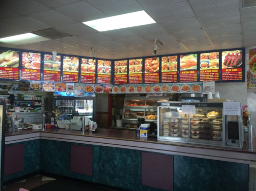 Interior of a fast-food restaurant with a menu board displaying various food items and a counter with food displays.