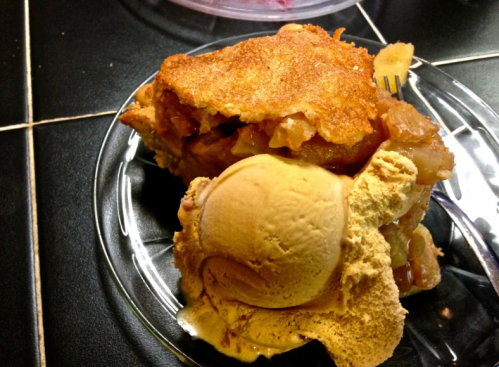 A slice of apple pie topped with a scoop of caramel ice cream on a glass plate.
