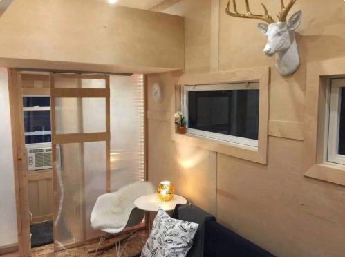 Cozy interior with wooden walls, a deer head mount, a small table, and a chair, featuring warm lighting and an air conditioner.