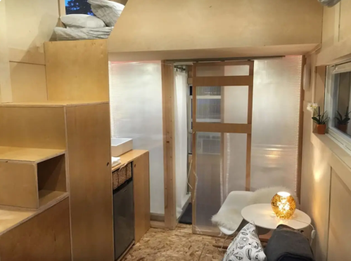 Cozy interior of a small space featuring wooden stairs, a kitchenette, and a seating area with soft lighting.