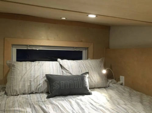 Cozy bedroom nook with a bed, striped pillows, a "smile" pillow, and soft lighting.