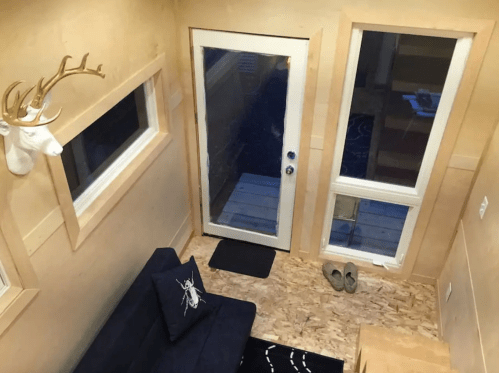 Cozy interior of a tiny home featuring a sofa, large windows, and a door leading to an outdoor deck.