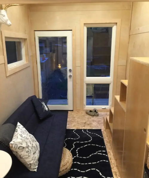 Cozy tiny home interior featuring a sofa, rug, shelves, and large windows for natural light.
