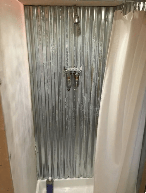 Shower stall with corrugated metal walls, a showerhead, and a curtain, featuring a simple faucet setup.