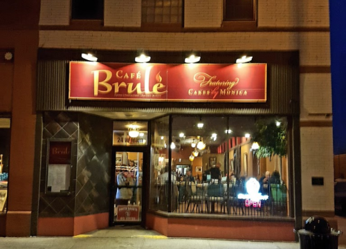 Exterior of Café Brûlé at night, featuring a lit sign and large windows showcasing the interior and seating.