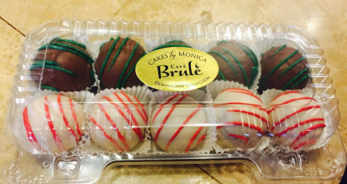 A clear plastic container holds assorted chocolate truffles, decorated with colorful drizzles and a label for Café Brûlé.