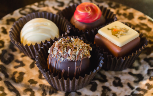 A plate of four assorted gourmet chocolates in decorative liners, featuring various toppings and designs.