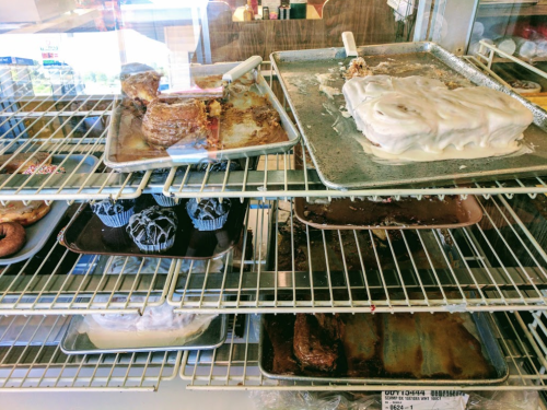 A display case filled with various baked goods, including cinnamon rolls, cupcakes, and frosted cakes.