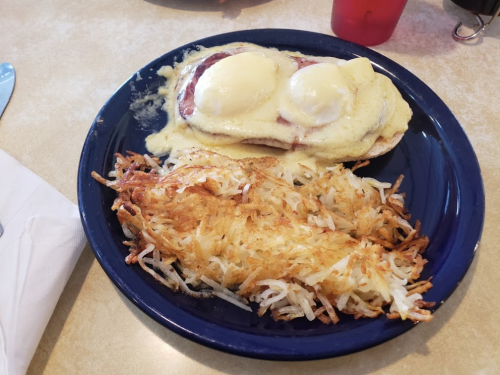 A blue plate with eggs Benedict topped with hollandaise sauce and a side of crispy hash browns.