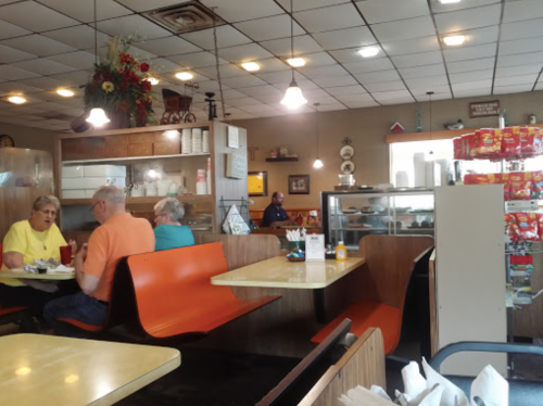 A cozy diner interior with orange booths, a display case, and customers enjoying their meals at tables.