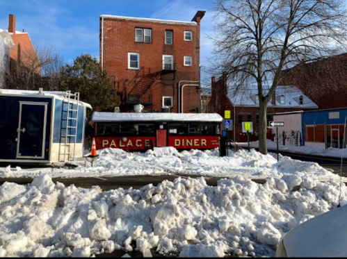 A diner named "Palace Diner" surrounded by snow, with a brick building and clear blue sky in the background.