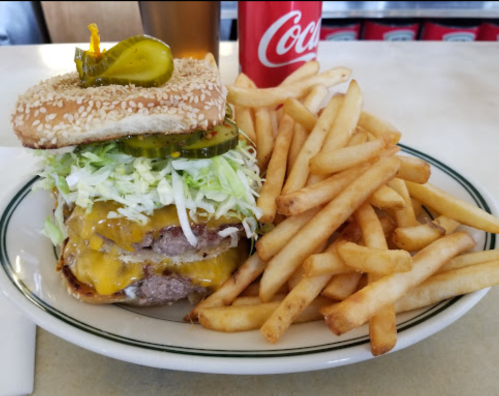 A large cheeseburger with lettuce and pickles, served with a side of fries and a Coca-Cola.