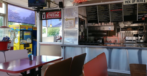 Interior of a diner with red tables, a counter, menu board, and a vintage arcade game in the background.